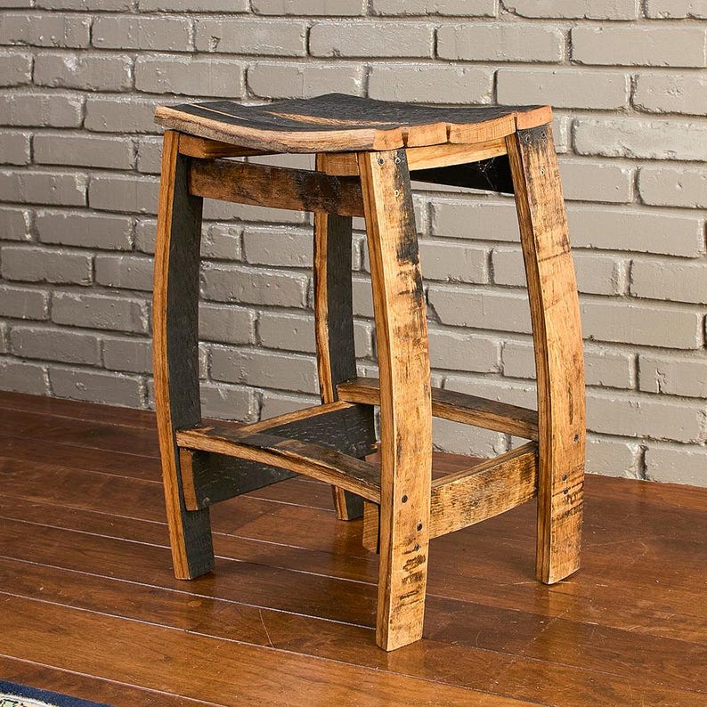 May include: A stool constructed from reclaimed oak wood barrel staves, featuring a curved seat and four legs connected by horizontal support braces. The wood displays natural grain patterns, light brown tones, and dark charred charcoal accents.