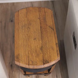 Op de afbeelding: Een bovenaanzicht van een kleine bijzettafel gemaakt van gebogen houten tonduigen. Het tafelblad heeft een natuurlijke lichtbruine houtnerf met zichtbare verticale naden tussen de planken en een donkere metalen band.
