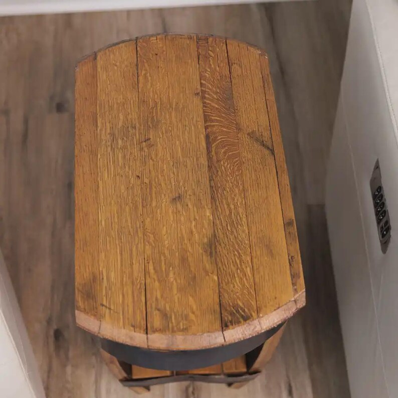 Op de afbeelding: Een bovenaanzicht van een kleine bijzettafel gemaakt van gebogen houten tonduigen. Het tafelblad heeft een natuurlijke lichtbruine houtnerf met zichtbare verticale naden tussen de planken en een donkere metalen band.