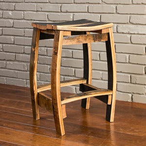 May include: A stool constructed from curved wooden barrel staves featuring a natural light brown wood grain finish on the interior sides and dark charred black wood on the exterior edges, with a rectangular seat and four sturdy legs.