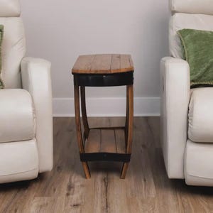 Op de afbeelding: Een kleine bijzettafel gemaakt van gebogen houten duigen en zwarte metalen banden. De tafel heeft een rechthoekig blad en een onderste plank, beide gemaakt van houten planken in natuurlijke tinten, ondersteund door vier gebogen poten.