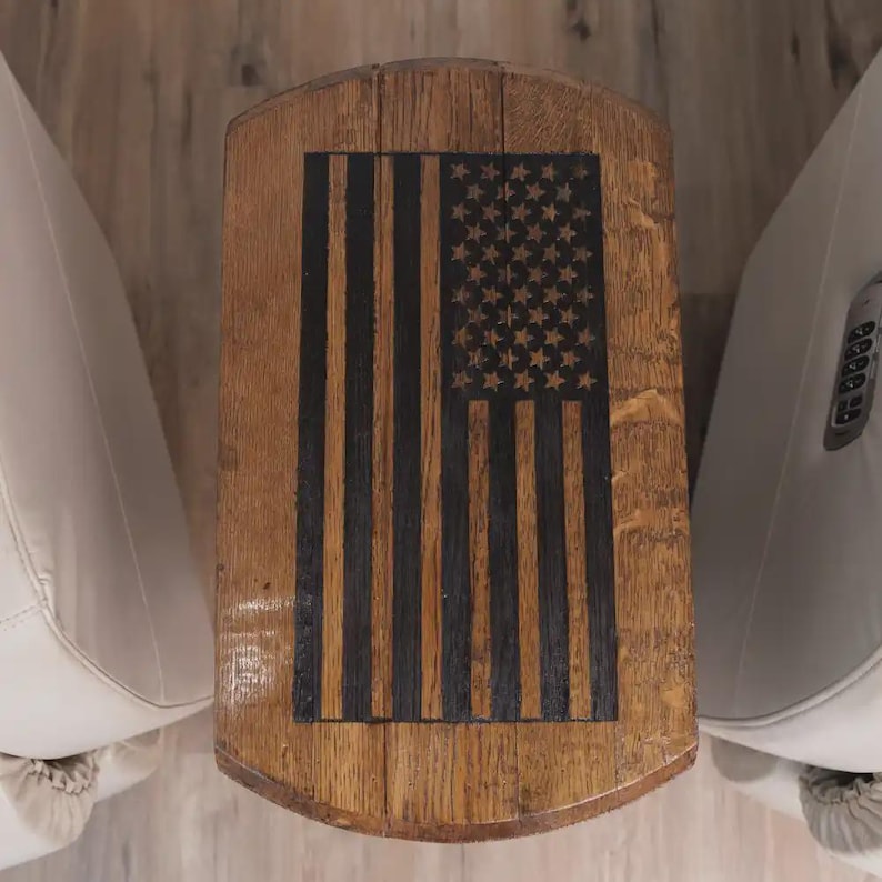 Op de afbeelding: Een tafelblad gemaakt van houten vatduigen met een donker gebeitst Amerikaans vlagontwerp. De natuurlijke houtnerf is zichtbaar rond de zwart geschilderde strepen en sterren, wat zorgt voor een contrast tussen het lichte hout en het motief.