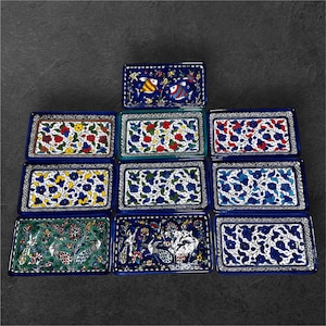 May include: A collection of rectangular ceramic dishes with intricate hand-painted designs. The dishes feature vibrant colors, including blue, red, yellow, and green, with floral and fish motifs. Each dish has a dark blue border.