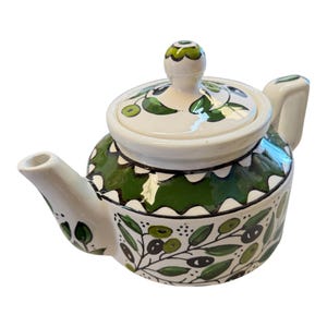 May include: A ceramic teapot with a white base and a green and black olive branch design. The lid and handle are white, and the lid features a green olive design. The teapot has a spout and a handle, and is suitable for serving tea.