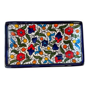 May include: Rectangular ceramic serving tray with a white background and a vibrant floral design. The flowers are red, blue, and orange, with green leaves and a dark blue border. A decorative piece for serving or display.