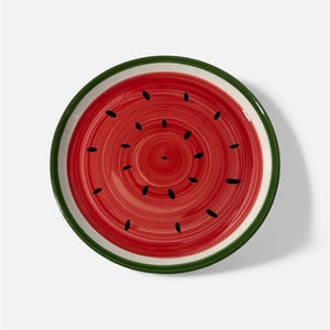 Pode incluir: Um prato redondo de cerâmica com um design de melancia. O prato apresenta um centro vermelho com detalhes de sementes pretas, uma borda branca e uma borda verde. O prato é projetado para se assemelhar a uma fatia de melancia.
