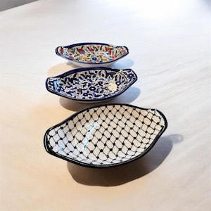 May include: Three decorative ceramic serving dishes. The top dish has a floral design with red, blue, and yellow accents. The middle dish features a blue and white floral pattern. The bottom dish has a black and white geometric design.