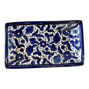 May include: Rectangular ceramic serving tray with a blue floral design on a white background. The tray has a dark blue border and features stylized blue flowers and leaves. A decorative piece for serving or display.