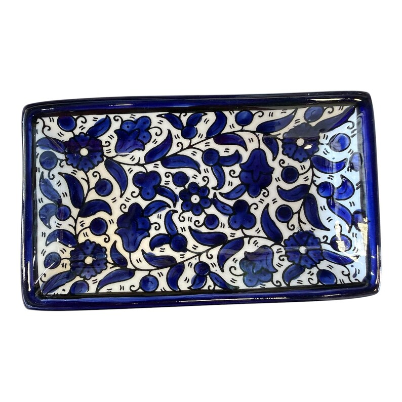 May include: Rectangular ceramic serving tray with a blue floral design on a white background. The tray has a dark blue border and features stylized blue flowers and leaves. A decorative piece for serving or display.