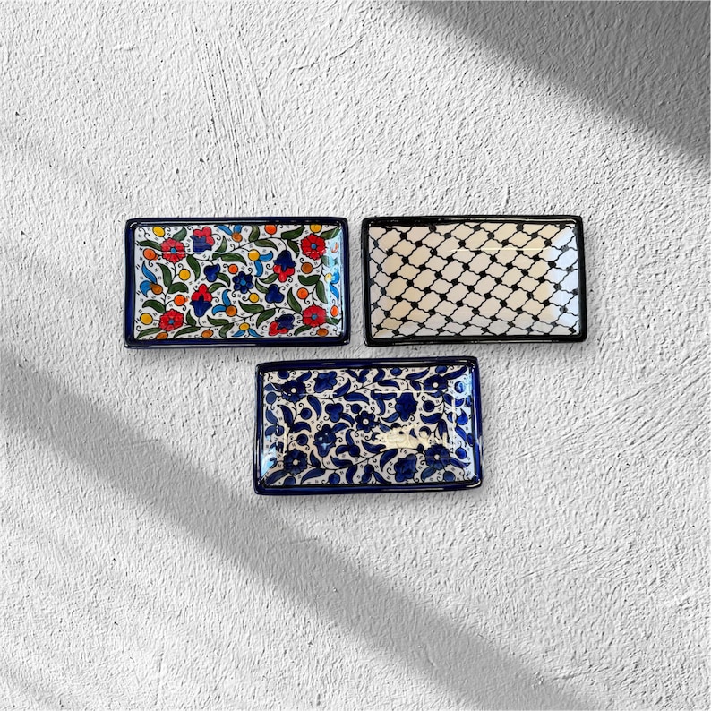 May include: Three rectangular ceramic dishes with decorative patterns. One features a floral design with red, blue, and yellow accents. Another has a black and white geometric pattern. The third has a blue and white floral design.