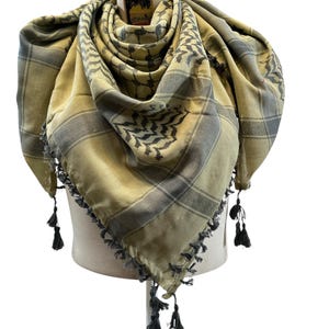 Può includere: Una sciarpa keffiyeh beige e grigia con un motivo a quadri e nappe decorative. La sciarpa è drappeggiata su una testa di manichino. La sciarpa ha un'etichetta attaccata.