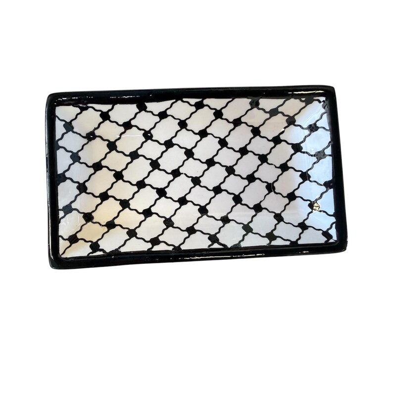 May include: Rectangular serving tray with a black and white geometric pattern. The tray has a black border and a repeating pattern of black shapes on a white background. The tray is likely made of ceramic or a similar material.