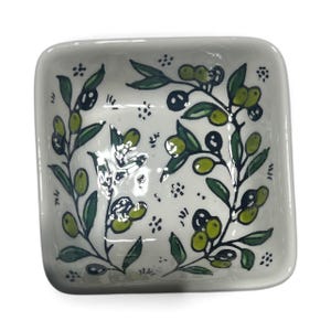 May include: Square ceramic dish with a white background, decorated with green olive branches and olives. The dish has rounded corners and a glossy finish. The olive branch design is repeated on all sides of the dish.