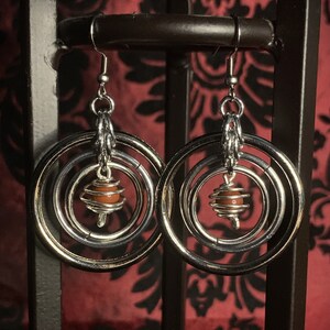 May include: Silver hoop earrings with multiple rings and a small orange bead in the center.