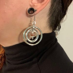 May include: Silver hoop earrings with a small, round, orange-brown bead in the center. The earrings are layered with three hoops of different sizes.