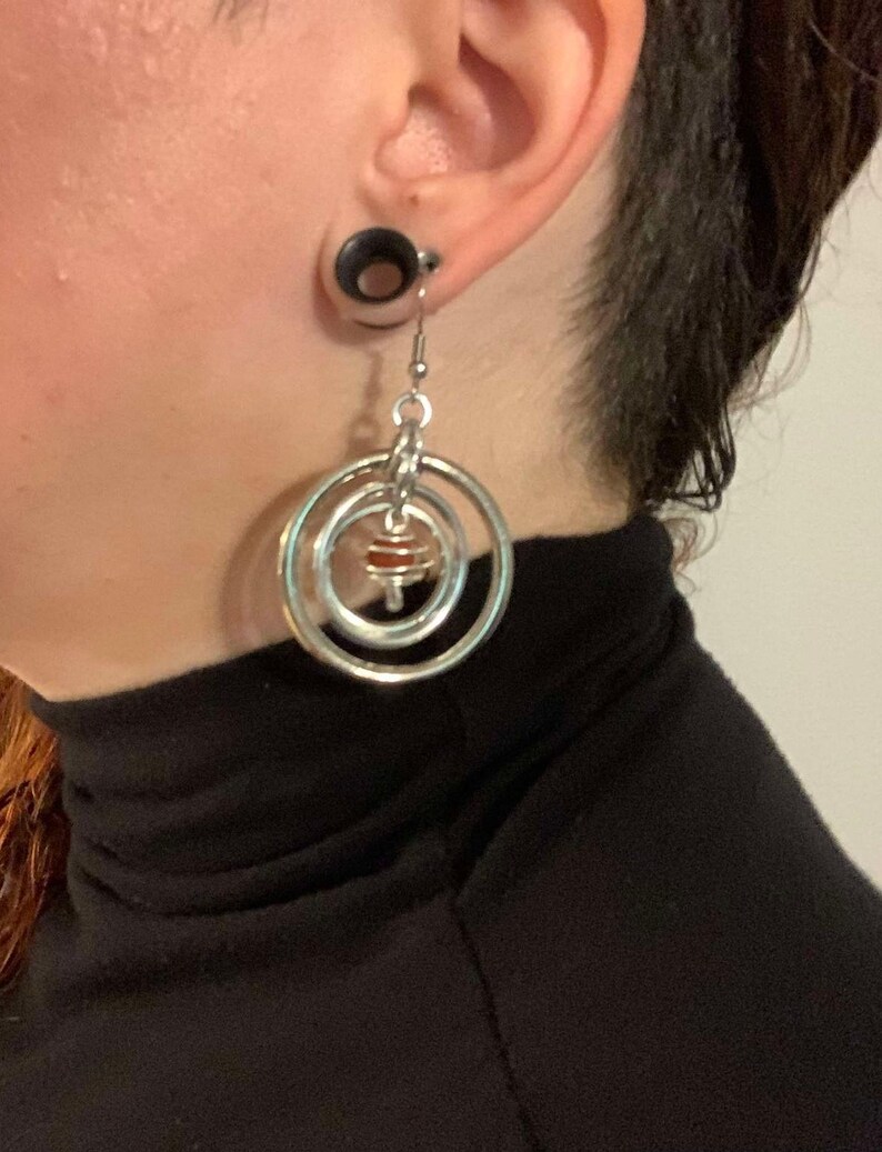 May include: Silver hoop earrings with a small, round, orange-brown bead in the center. The earrings are layered with three hoops of different sizes.