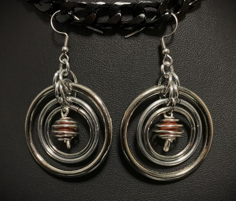May include: Silver hoop earrings with three concentric circles and a brown bead in the center.
