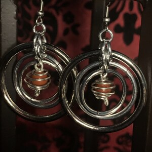 May include: Silver hoop earrings with three concentric circles and a red gemstone encased in a wire cage hanging from the center.