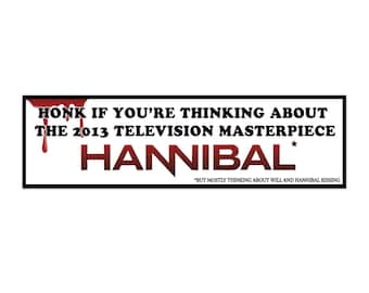 May include: A rectangular bumper sticker with a black border and white background. The text reads "HONK IF YOU'RE THINKING ABOUT THE 2013 TELEVISION MASTERPIECE HANNIBAL". Red blood-like drips and text accents are included.