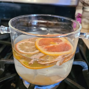 May include: A glass jar containing dried orange slices and water is on a hob with a blue flame.