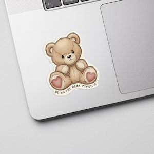 May include: A sticker featuring a light brown teddy bear with a heart-shaped design on its paws. The bear is sitting with its legs spread. The text "DOING THE BEAR MINIMUM" is written in a circular pattern below the bear.