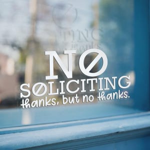 May include: A white vinyl sticker on a glass door that reads "NO SOLICITING thanks, but no thanks."