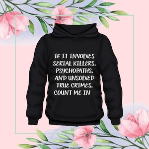 Puede incluir: Sudadera con capucha negra con el texto blanco: "IF IT INVOLVES SERIAL KILLERS, PSYCHOPATHS, AND UNSOLVED TRUE CRIMES, COUNT ME IN". El diseño está sobre un fondo rosa con adornos florales.