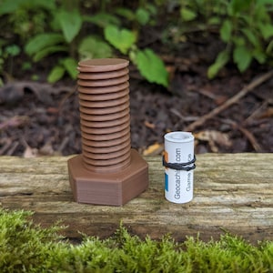 May include: A brown plastic bolt-shaped container with a black rubber band around it. The container is labeled "Geocaching.com Game On".