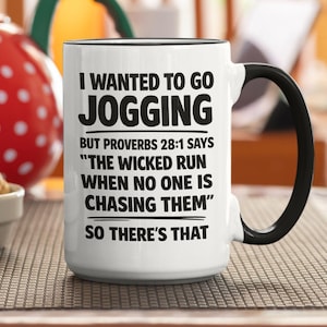 May include: A white ceramic mug with a black handle and interior rim. The mug features black printed text that reads: I WANTED TO GO JOGGING BUT PROVERBS 28:1 SAYS THE WICKED RUN WHEN NO ONE IS CHASING THEM SO THERE'S THAT. The mug has a cylindrical shape.