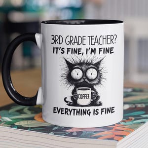 Puede incluir: Taza de cerámica blanca con interior y asa negros. La taza presenta una ilustración caprichosa de un gato negro sosteniendo una taza de café, con el texto "3rd Grade Teacher? It's Fine, I'm Fine, Everything is Fine."