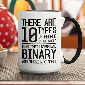 Puede incluir: Taza de cerámica blanca con asa y borde negros. La taza presenta el texto "THERE ARE 10 TYPES OF PEOPLE IN THE WORLD, THOSE THAT UNDERSTAND BINARY AND THOSE WHO DON'T" en fuente negra.