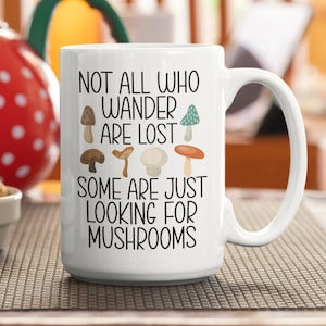 May include: White ceramic mug with a black and white design that reads "Not all who wander are lost, some are just looking for mushrooms". The design also features a variety of colorful mushrooms.
