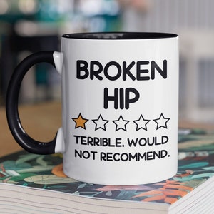 May include: White ceramic mug with a black handle and rim. The mug features the text "BROKEN HIP" above a one-star rating and the phrase "TERRIBLE. WOULD NOT RECOMMEND."