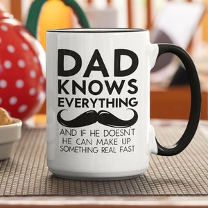 Peut inclure: Une tasse en céramique blanche avec une poignée noire. La tasse est ornée d'un texte noir qui dit "Dad Knows Everything" avec une moustache noire en dessous. Le texte sous la moustache dit "And if he doesn't he can make up something real fast."