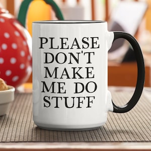 May include: White ceramic mug with black handle and rim. The mug features the text "PLEASE DON'T MAKE ME DO STUFF" in black, centered on the front. A red and white polka-dotted teapot and a small bowl of cookies are in the background.