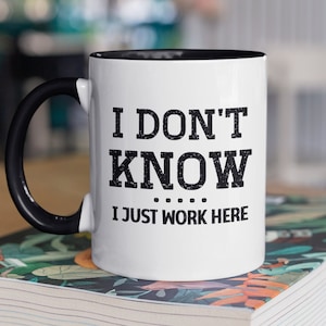 May include: White coffee mug with a black handle and black rim. The mug has black text that reads "I don't know... I just work here."