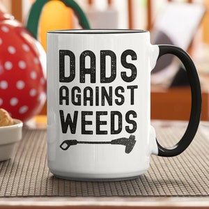 May include: White ceramic mug with a black handle. The mug has black text that reads "Dads Against Weeds" with a weed whacker graphic.