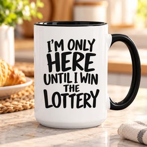 Puede incluir: Una taza de cerámica blanca con interior y asa de color negro. El frente de la taza presenta un texto en negrita de color negro que dice: I'M ONLY HERE UNTIL I WIN THE LOTTERY. La taza tiene una forma cilíndrica y un acabado brillante.