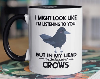 May include: White coffee mug with a black rim and handle. The mug has a black crow illustration and the text "I might look like I'm listening to you, but in my head I'm thinking about crows."