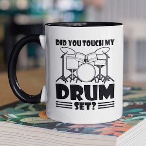 May include: White ceramic mug with a black handle and black rim. The mug has a black graphic of a drum set with the text "Did you touch my drum set?"