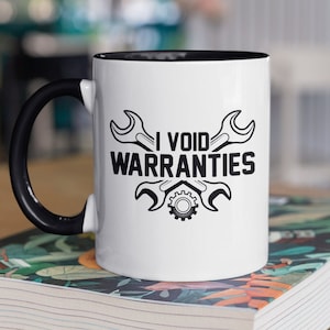May include: White ceramic mug with a black handle and black rim. The mug has a black graphic of two wrenches and a gear with the text "I VOID WARRANTIES".