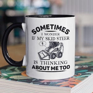 May include: White ceramic mug with a black handle and black rim. The mug has a black graphic of a skid steer with the text "Sometimes I wonder if my skid steer is thinking about me too."