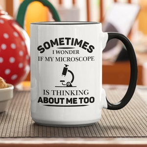 May include: White ceramic mug with a black handle. The mug has black text that reads "Sometimes I wonder if my microscope is thinking about me too." A black and white illustration of a microscope is included in the text.