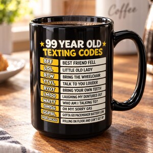 以下が含まれることがあります： 黒いセラミック製のマグカップで、黄色と白の文字で「99 YEAR OLD TEXTING CODES」と書かれ、その後にBFF（Best Friend Fell）、LOL（Little Old Lady）、ROFLACGU（Rolling On Floor And Can't Get Up）などのユーモラスな頭字語とその定義がリストされています。