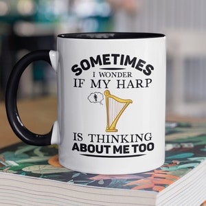 May include: White ceramic mug with a black handle and black rim. The mug has a black graphic that says "Sometimes I wonder if my harp is thinking about me too." The graphic includes a cartoon harp with a thought bubble above it showing a person.