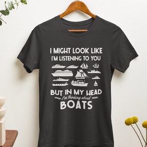 May include: A dark gray t-shirt with a white graphic design. The graphic features a variety of boat silhouettes and the text "I might look like I'm listening to you, but in my head I'm thinking about BOATS."