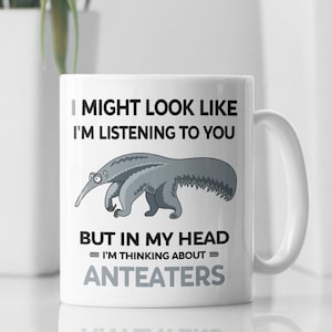 Op de afbeelding: Een witte keramische mok met een zwart-grijze illustratie van een miereneter. De mok heeft de tekst "I might look like I'm listening to you, but in my head = I'm thinking about = anteaters".