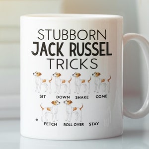 May include: White ceramic mug with a black graphic of a Jack Russell Terrier and the text "Stubborn Jack Russel Tricks". The graphic shows the dog in different poses, with the text "Sit", "Down", "Shake", "Come", "Fetch", "Roll Over", and "Stay" below each pose.
