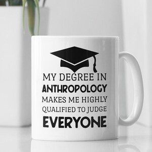 Può includere: Tazza da caffè in ceramica bianca con un grafico di cappello di laurea nero e il testo "La mia laurea in antropologia mi rende altamente qualificato per giudicare tutti".