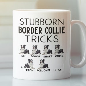 May include: White ceramic mug with the text "STUBBORN BORDER COLLIE TRICKS" and illustrations of a Border Collie performing tricks. The tricks include sit, down, shake, come, fetch, roll over, and stay. The mug has a white handle.